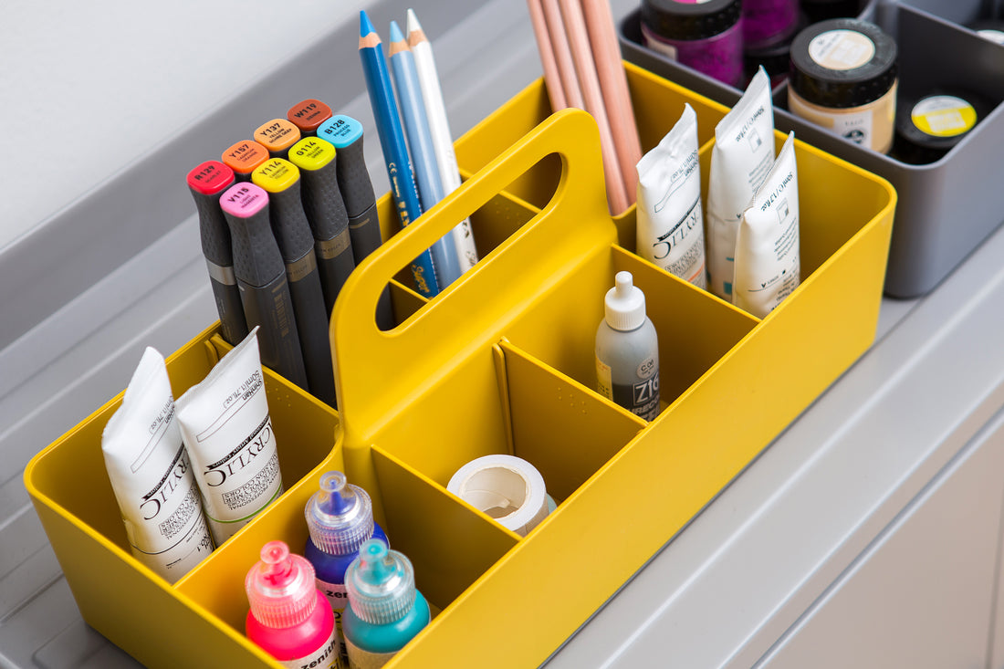 Yellow plastic storage caddy filled with various art supplies including markers, pencils, and paints.